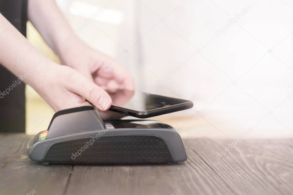 Female paying with smart phone, hands close up. Woman using mobile phone for pay by the bill in a restaurant 