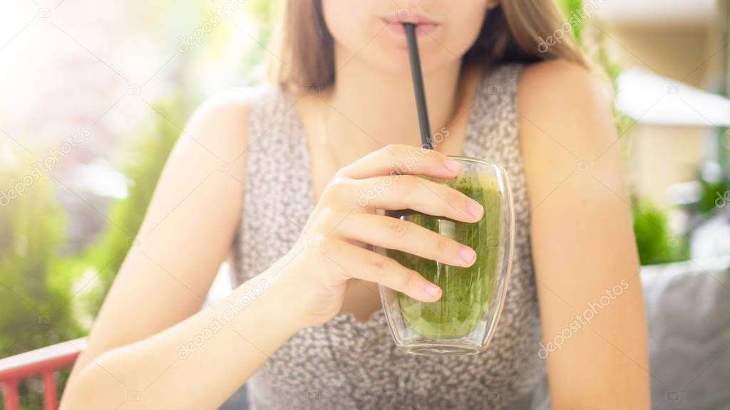 A girl holds a tasty green smoothie. Female hand holding smoothie. young girl drinking green smoothie with a straw 