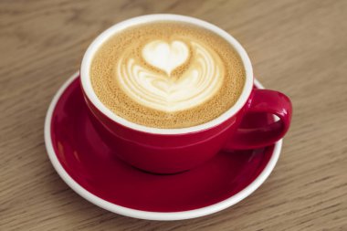 Ahşap bir masada kapuçino ile kırmızı fincan. 