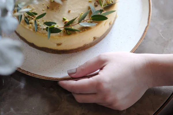 Bolo de queijo festivo em uma mesa em um café. Bolo de queijo com manga e pistache. Uma menina segura um prato com um cheesecake . — Fotografia de Stock