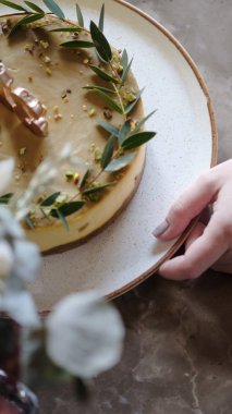 Bir kafede bir masada şenlikli cheesecake. Mango ve antep fıstığı ile Cheesecake. Bir kız cheesecake ile bir tabak tutar.
