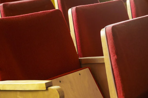 Old tired cinema seats covered with worn red velvet. Empty red chairs in theatre.