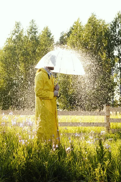 A man in a yellow raincoat in the rain.  It\'s raining and the sun is shining.