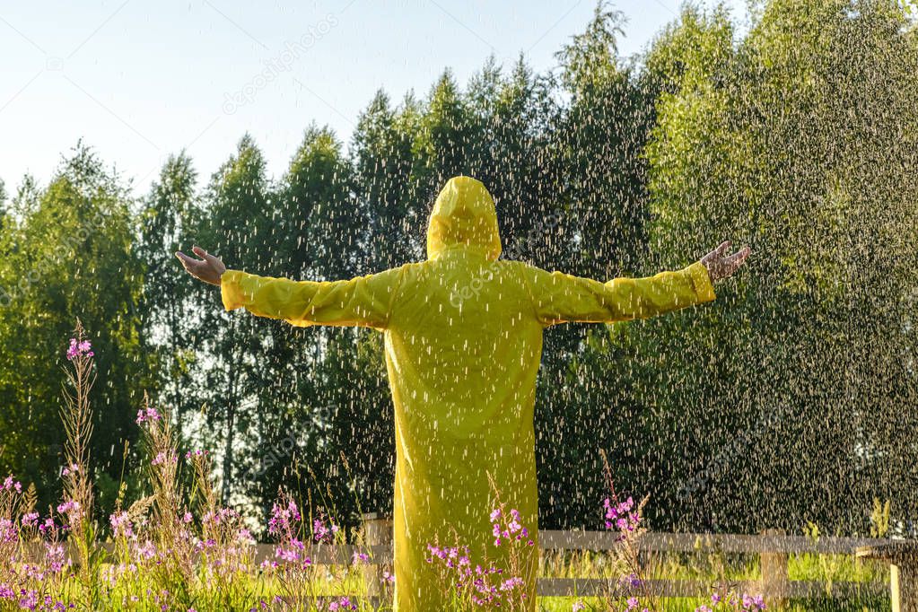 A man in a yellow raincoat stands in the rain and looks forward, raising his hands to the sky. concept of nature and happy life. Adventure, purity. 