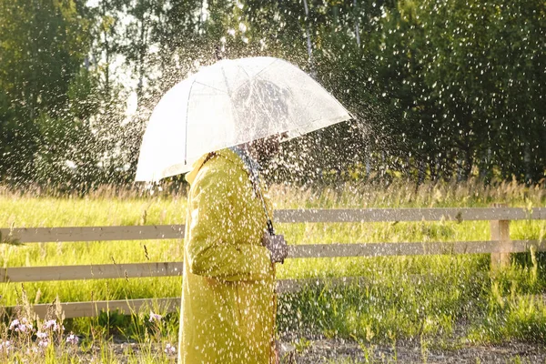 Un uomo con un impermeabile giallo sotto la pioggia. Sta piovendo e il sole splende . — Foto Stock