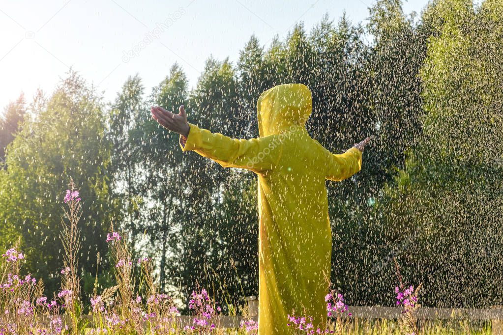 A man in a yellow raincoat stands in the rain and looks forward, raising his hands to the sky. Adventure, purity. 