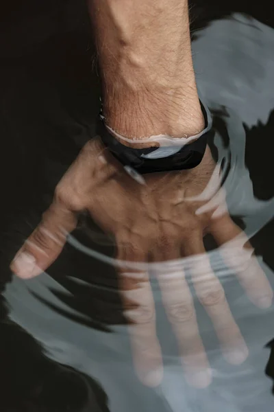 Pulsera impermeable de fitness en una mano masculina. Compruebe pulsera inteligente para la resistencia al agua. Mano masculina en el agua . — Foto de Stock