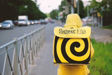 Kazan, Russia - June 07, 2020: Yandex Food - food delivery service. Courier or delivery man with a yellow backpack on a bicycle. Yandex eda. clipart