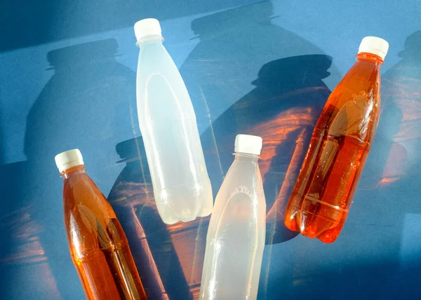 Plastic bottles of sparkling water in orange and white color with hard shadows lie on a blue background. The concept of summer and summer mood. Blue and orange are a contrasting color combination.