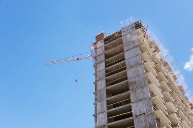 Apartman blokları inşa edilirken bir inşaat alanındaki vinç kulesi. İnşaat halindeki konutların detayları. Metal destekli beton yapı ve geçici ahşap korkuluklar