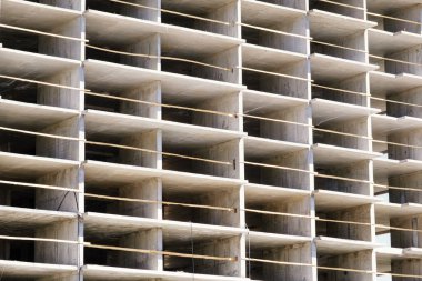 İnşaat halindeki konutların detayları. Metal destekli beton yapı ve geçici ahşap korkuluklar. Bulutlu mavi gökyüzüne karşı inşa halinde olan yüksek binalar.