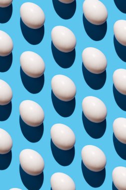 Pastel mavi arka planda yumurtadan yapılmış desen. Asgari gıda konsepti. Moda olmayan şekilli yumurtaların yassılaşması..