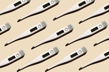 Pastel bej arka planda izole edilmiş elektronik modern termometrelerin deseni. Ateş teşhisi, tıbbi muayene ve sağlık konsepti