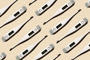 Pastel bej arka planda izole edilmiş elektronik modern termometrelerin deseni. Ateş teşhisi, tıbbi muayene ve sağlık konsepti