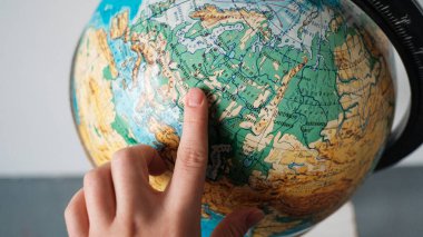 The girl points to a location on the world globe. Chooses a place to travel on the globe. clipart