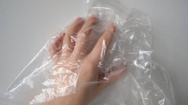 Plastik Torbanın Arkasında Kırpılmış El. Beyaz renkte şeffaf plastik torba üzerinde buruşuk yüzeye dokunan isimsiz birinin el silueti. Seçici odak