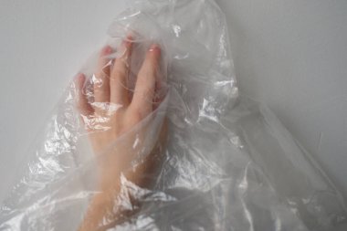 Plastik Torbanın Arkasında Kırpılmış El. Beyaz renkte şeffaf plastik torba üzerinde buruşuk yüzeye dokunan isimsiz birinin el silueti. Seçici odak