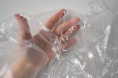 Plastik Torbanın Arkasında Kırpılmış El. Beyaz renkte şeffaf plastik torba üzerinde buruşuk yüzeye dokunan isimsiz birinin el silueti. Seçici odak