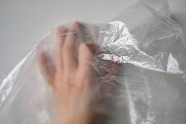 Plastik Torbanın Arkasında Kırpılmış El. Beyaz renkte şeffaf plastik torba üzerinde buruşuk yüzeye dokunan isimsiz birinin el silueti. Seçici odak