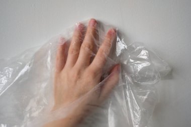 Plastik Torbanın Arkasında Kırpılmış El. Beyaz renkte şeffaf plastik torba üzerinde buruşuk yüzeye dokunan isimsiz birinin el silueti. Seçici odak