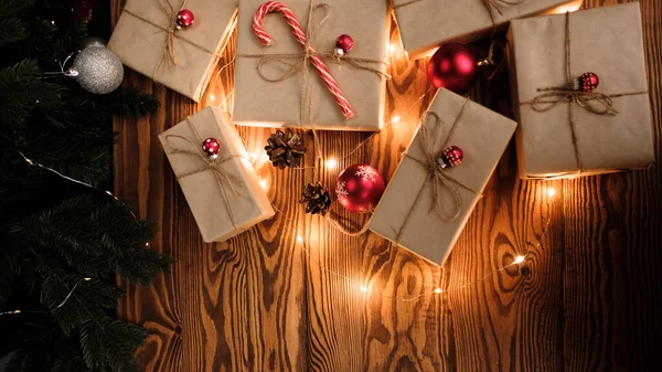 Kraft kağıdına sarılı yeni yıl hediyeleri ve Noel şekeri ve tahta arka planda kırmızı Noel oyuncağı ile süslenmiş. Noel arkaplanı. Mutlu yıllar.