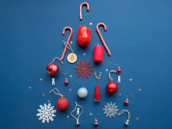 Noel ağacı şeklinde dizilmiş Noel nesneleri, tepeden bakıldığında. Kırmızı Noel oyuncakları, kar taneleri, Noel şekerlemeleri ve mavi arka planda diğer tatil dekorlarıyla bezenmiş düz bir kompozisyon..