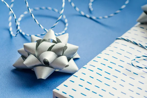 Gift packaging: silver bows for gift decoration, blue gift rope, gift in a white box on a blue background. Preparing for Christmas holidays. Selective focus
