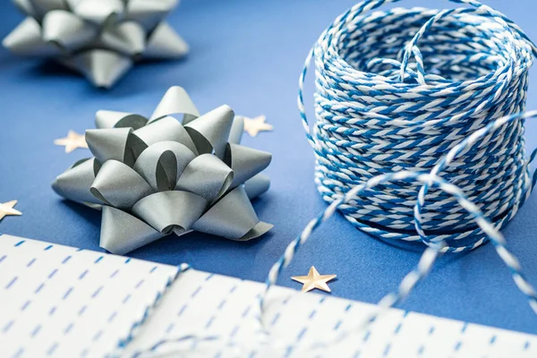 Gift packaging: silver bows for gift decoration, blue gift rope, gift in a white box on a blue background. Preparing for Christmas holidays. Selective focus