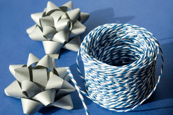 Gift packaging: silver bows for gift decoration and blue gift rope on a blue background. Preparing for Christmas holidays. Selective focus