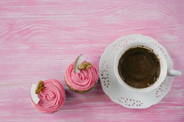 İki top kek bir pembe şanti buttercream, düzenlenen Hindistan cevizi bir parça ve bir üst ve beyaz fincan kahve üzerinde ceviz parçası ile süslenmiş