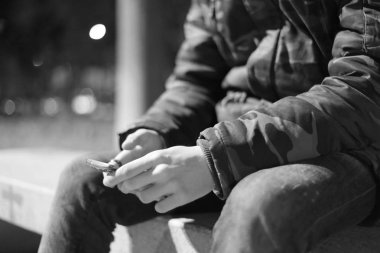 Adam şehir parkında bankta otururken akıllı telefon kullanıyor. 