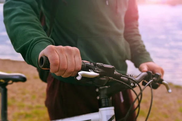 Male hands on a bicycle handle close up at sunset. A man with a bicycle