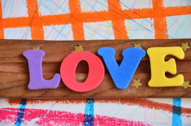 Aşk kelimesi ahşap bir arka planda renkli harflerden oluşur.