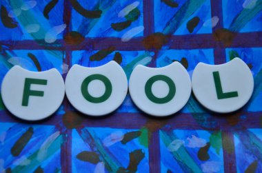 word april made of wooden letters on a blue background with green leaves.