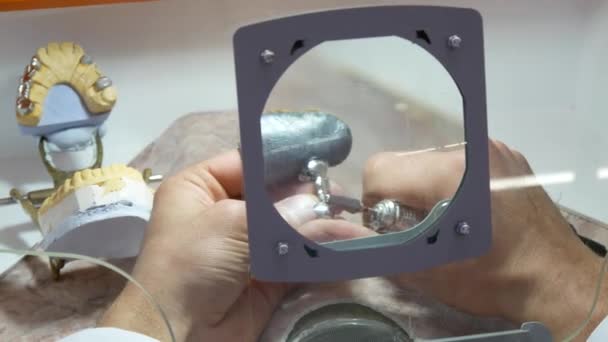 Tandtechnicus maalt de metalen frame door middel van een vergrootglas — Stockvideo