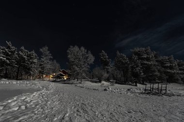 Finlandiya, Inari - Ocak 2019: Donmuş gölün kenarındaki Otel'den Gelen ışıkları karşılayan, mehtaplı kış manzarası