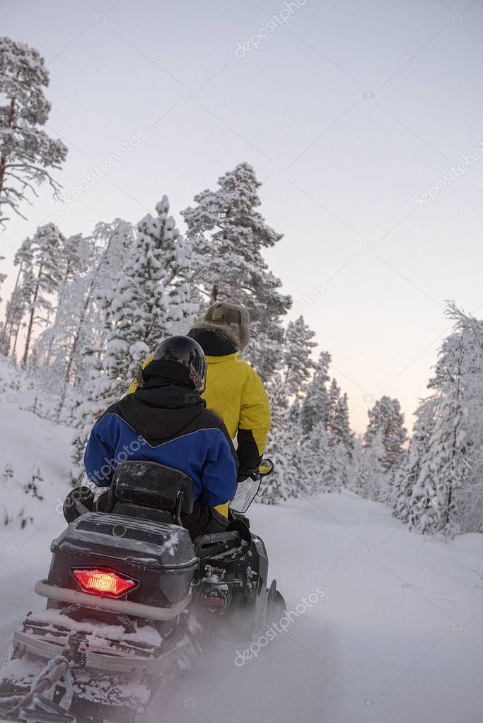 2 people riding on a snowmobile through the wilds of Lapland
