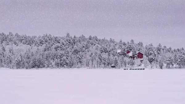 Červený dům se sněhovými mobily venku, když padá sníh — Stock fotografie
