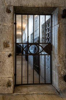 Venedik, İtalya - Mart 2024: Demir parmaklıklı bir kapı, Doge Palace cezaevi kompleksinde, hücre kapılarının taş duvarlar boyunca uzandığı loş bir koridora açılıyor