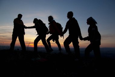 Turist günbatımında bir dağın tepesinde bir grup.