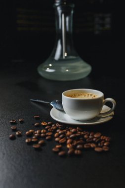 Espresso kahve krematoryum ve dağınık kahve çekirdekleri bir siyah arka plan ve duman içinde belgili tanımlık geçmiş.