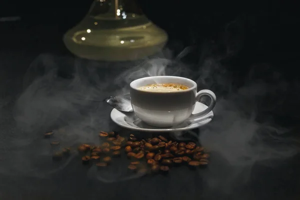 Кофе эспрессо с кремом и разбросанные кофейные зерна на черном фоне и дым на заднем плане . — стоковое фото