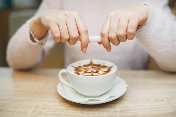 Female hand pours sugar into coffee.