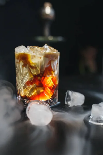 Iced karamell cocktail i ett glas med sirap, is och vispad grädde. Svart bakgrund och rök — Stockfoto
