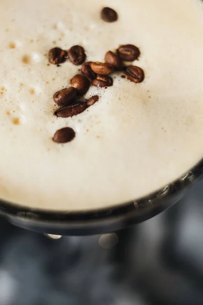 Glas med kaffe drink, vit crema, kaffebönor, svart bakgrund, isbitar. Närbild. Ovanifrån — Stockfoto