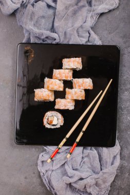 Sushi Set nigiri ve suşi rulo olarak soya sosu, demir demlik ve çubuk siyah taş doku arka plan üzerinde koyu seramik tabak. Üstten Görünüm alanına sahip. Japonya menü. Kare görüntü