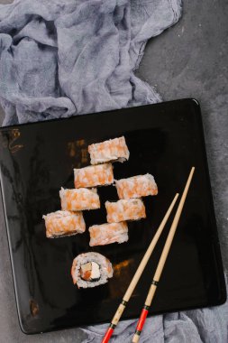 Sushi Set nigiri ve suşi rulo olarak soya sosu, demir demlik ve çubuk siyah taş doku arka plan üzerinde koyu seramik tabak. Üstten Görünüm alanına sahip. Japonya menü. Kare görüntü
