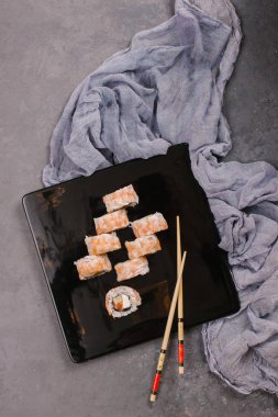 Sushi Set nigiri ve suşi rulo olarak soya sosu, demir demlik ve çubuk siyah taş doku arka plan üzerinde koyu seramik tabak. Üstten Görünüm alanına sahip. Japonya menü. Kare görüntü