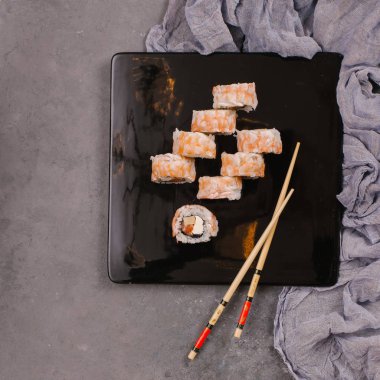 Sushi Set nigiri ve suşi rulo olarak soya sosu, demir demlik ve çubuk siyah taş doku arka plan üzerinde koyu seramik tabak. Üstten Görünüm alanına sahip. Japonya menü. Kare görüntü