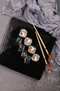 Sushi Set nigiri ve suşi rulo olarak soya sosu, demir demlik ve çubuk siyah taş doku arka plan üzerinde koyu seramik tabak. Üstten Görünüm alanına sahip. Japonya menü. Kare görüntü